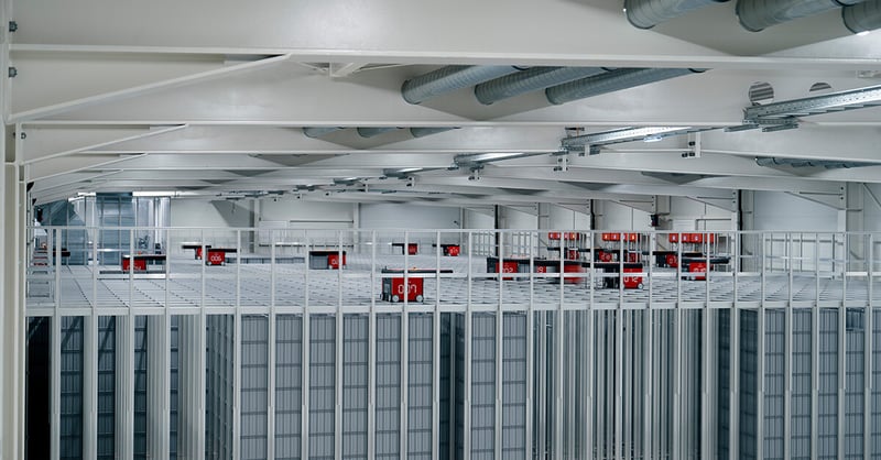 Red robots moving on top of a metal storage grid in a large warehouse