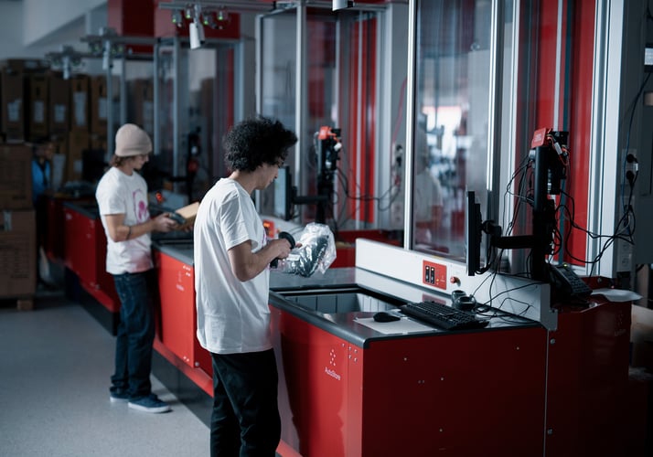 Two men picking items out of totes at red workstation inside a warehouse